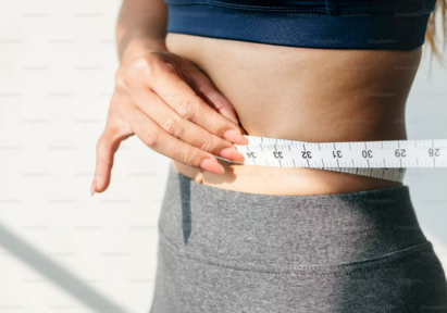 A woman measuring her waist size with a measuring tape.
